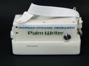 Front and top view of Second Generation Palm Writer seated on Charging Station, Palm Write top plate shows the words "Morgan Dynamic Research" in light blue, and the words "Palm Writer" beneath the first in middle dark green