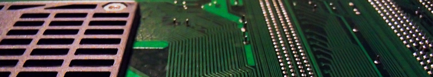 Closeup of the bottom of a computer motherboard. Metallic green PCB lined with various depths of darker green wires with rows of shining silver solder points. Ruddy brown base of a heat sink mount visible to the left of the frame