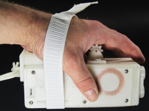 A Palm Writer being properly gripped by a hand with aid of the ergonomic hand strap in a left handed manner as shown from the charging side.