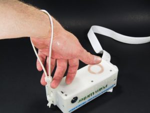 A hand inserted through a wrist strap on a Palm Writer pulling up the tensioner using the third and fourth fingers.
